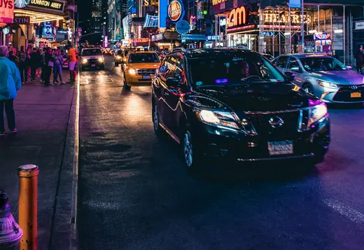 Black SUV on Broadway at night under the Times Square theater lights